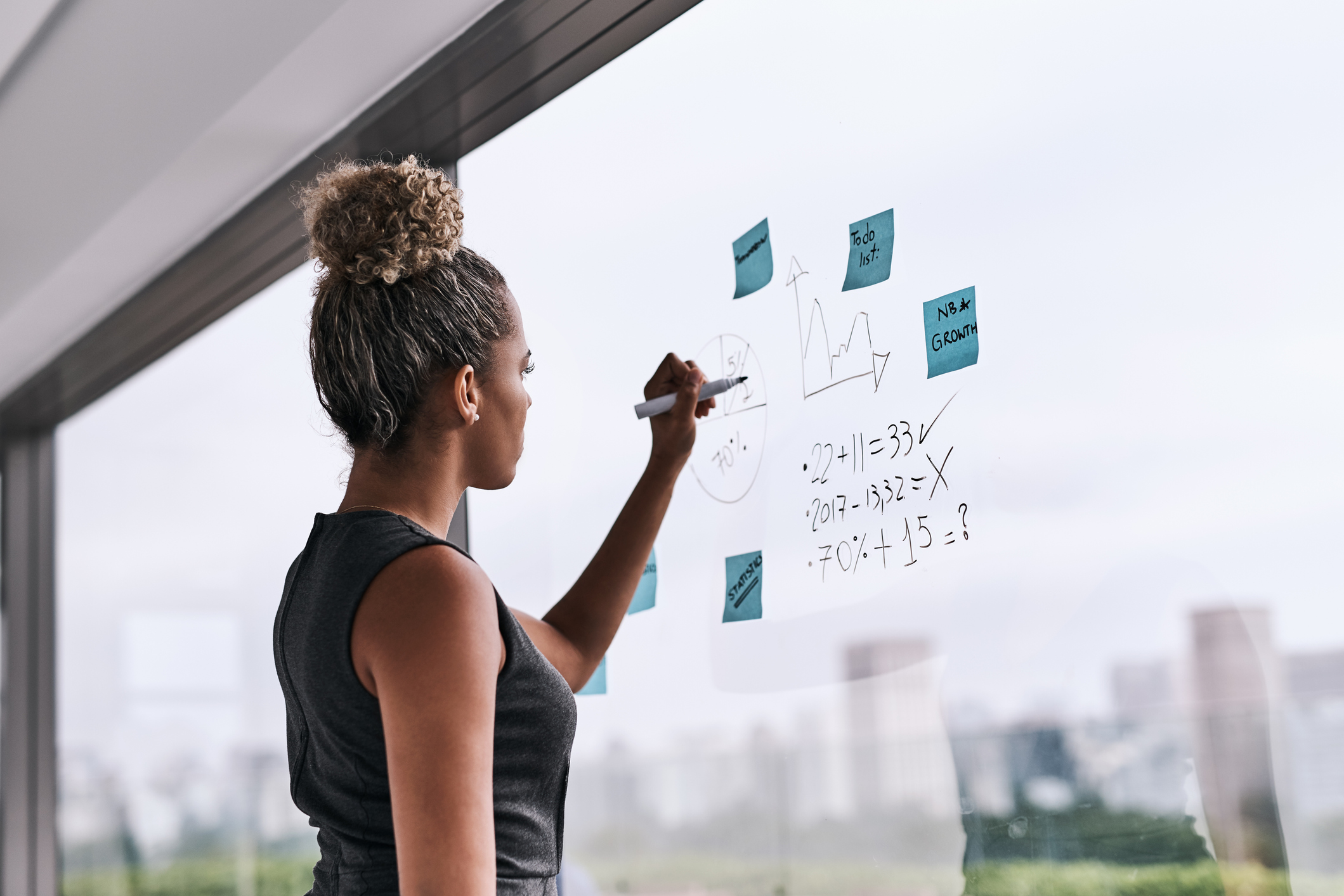 a young businesswoman writing on a glass wall in an office
