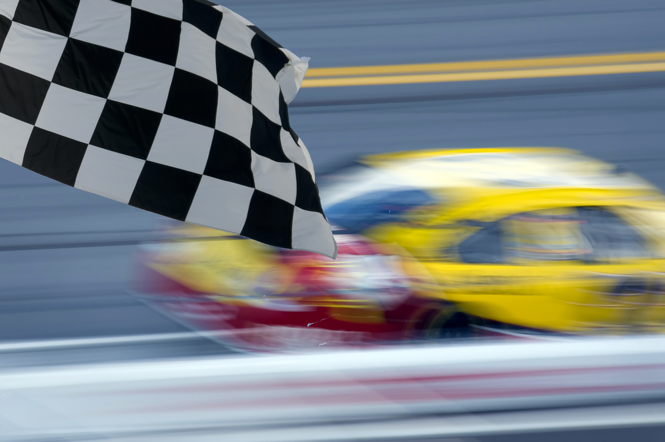 race car blurred on track against rail, checkered flag in foreground