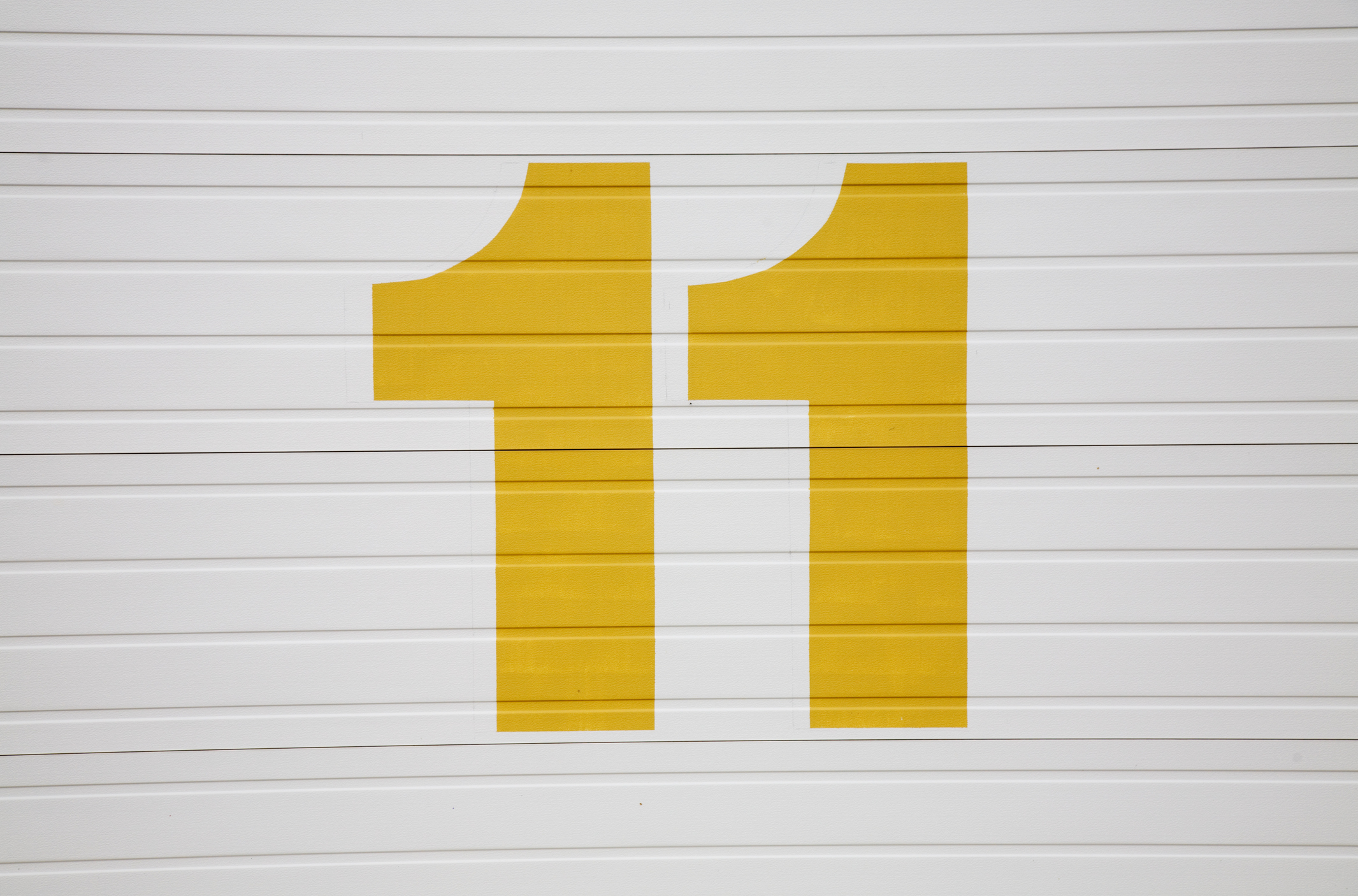 Yellow numeral 11 painted on a White wooden background