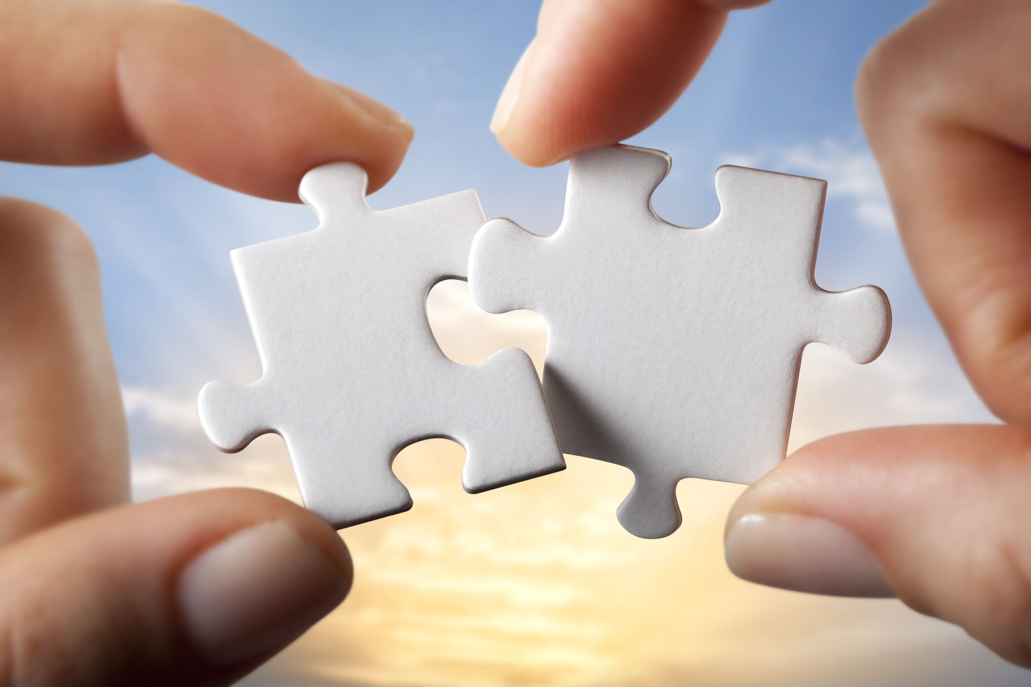 Two hands putting two white puzzle pieces together.