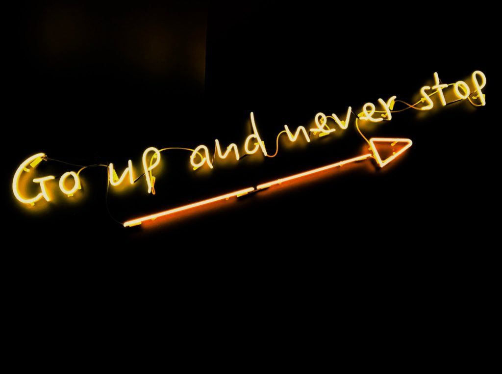Neon sign with an arrow, reading "Go up and never stop."