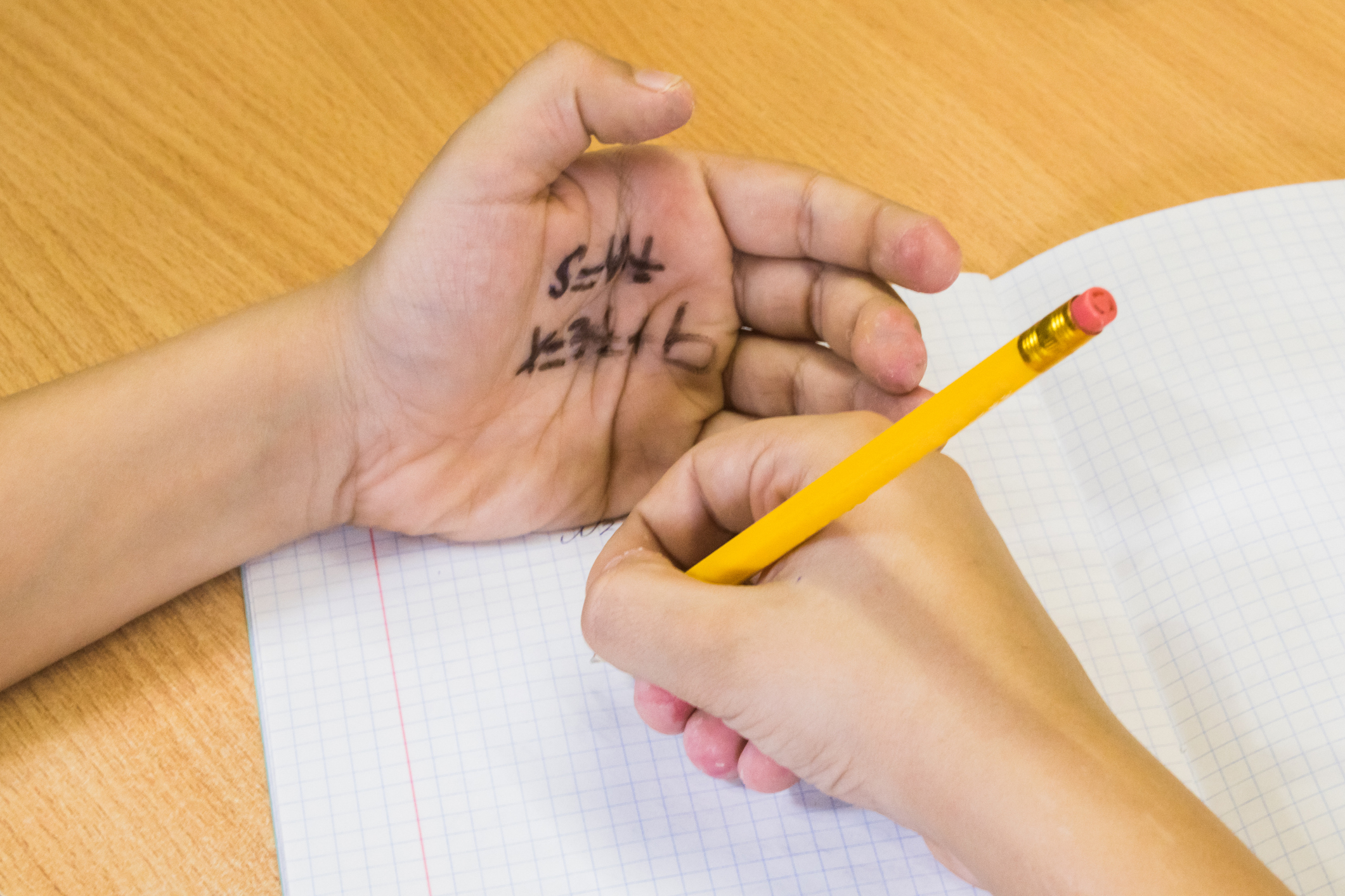 Student taking an exam with a formula written on the palm of a hand