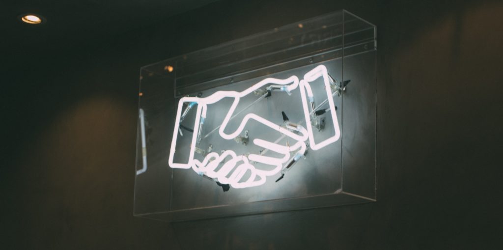 Image of a neon sign depicting two hands shaking.