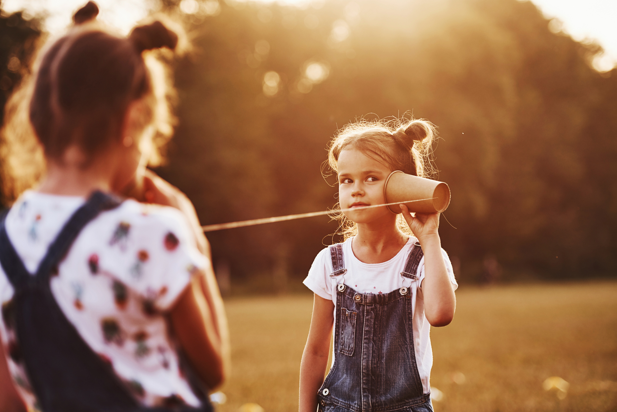 Two young girls communicating with two tin cans on each end of a string.