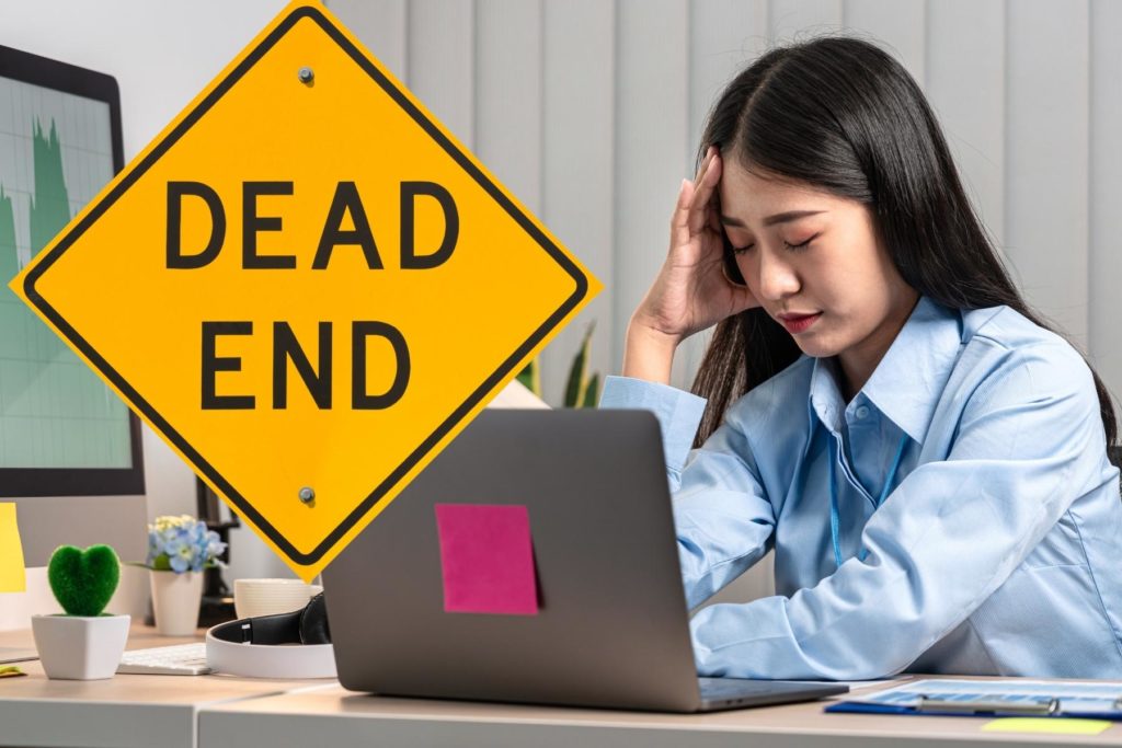 Frustrated worker sitting at her desk, holding her head in her hand.