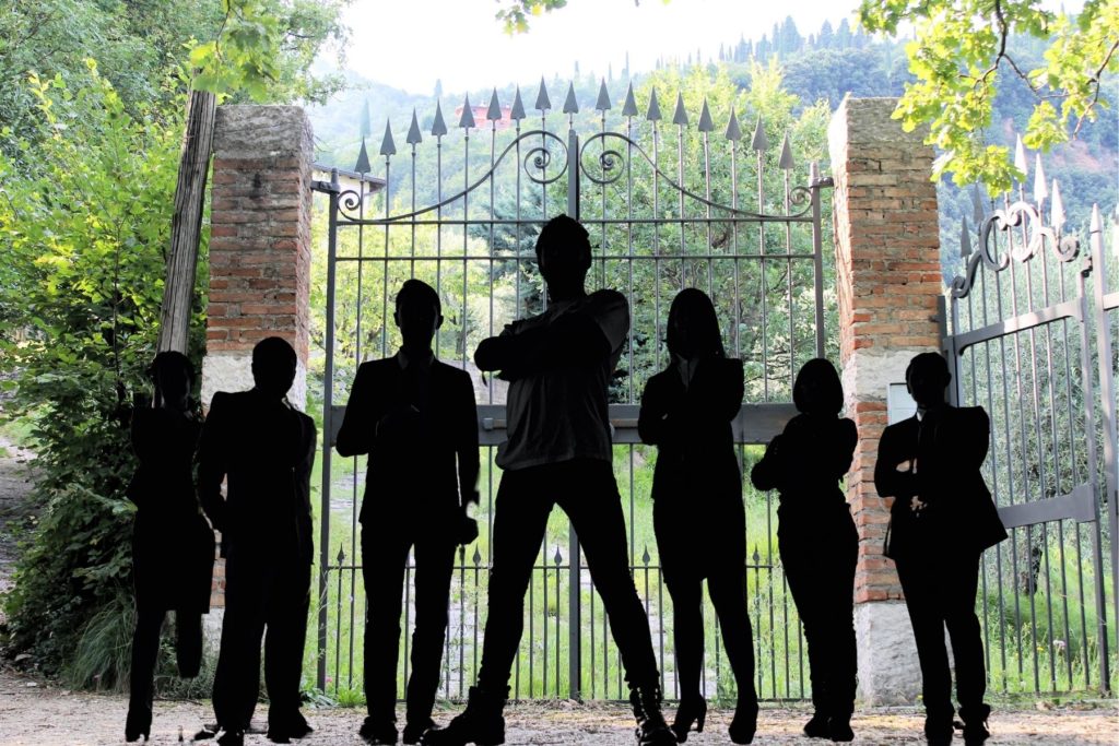 Image of seven human silhouettes standing in front of a gate. 