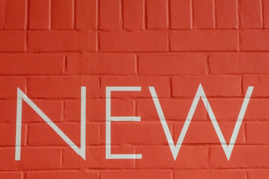 The word 'new' painted in white on an orange brick wall. 