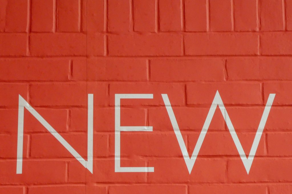 The word 'new' painted in white on an orange brick wall. 