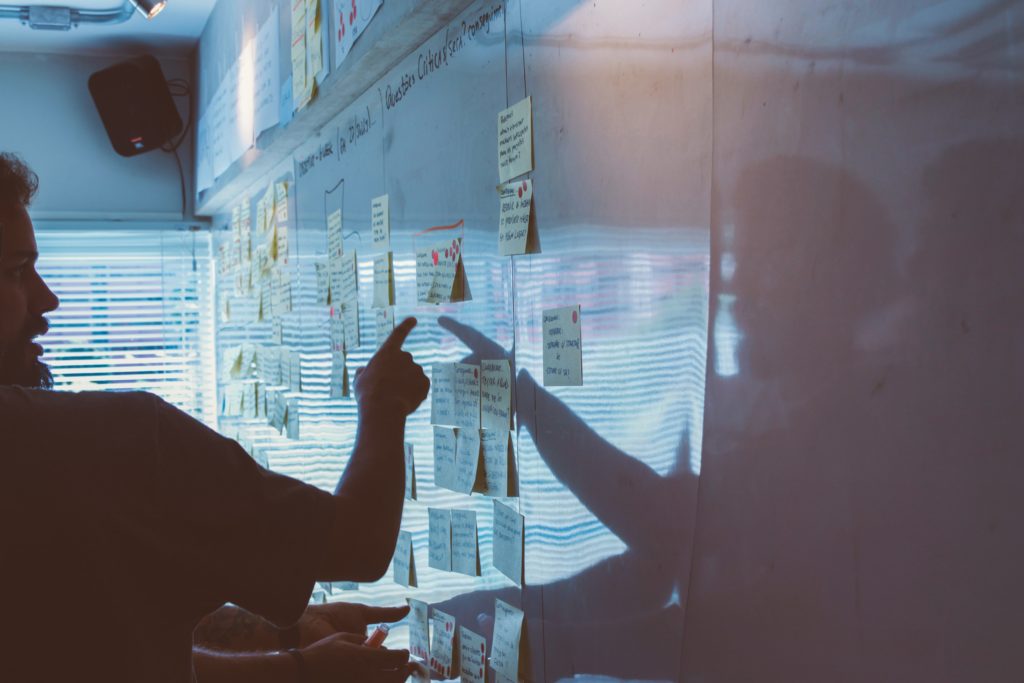 Man pointing to an array of sticky notes on a whiteboard. 