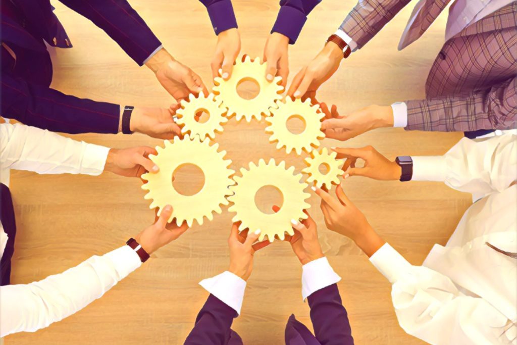 A business team holding gears in their outreached hands, meshing them together.