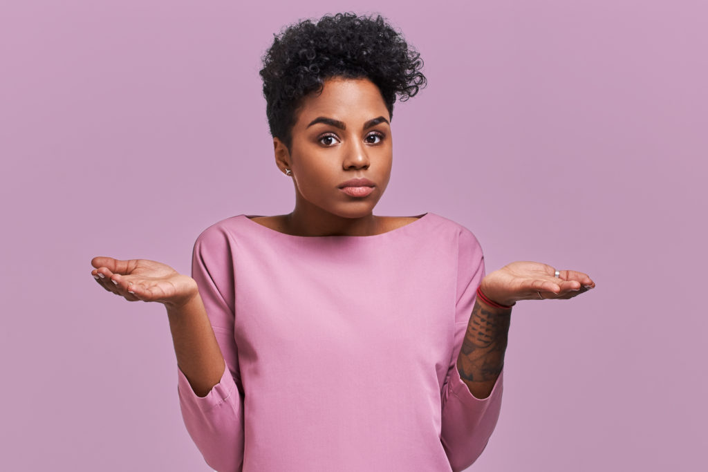 Woman standing, shrugging her shoulders, with each hand turned upward, indecisively weighing one option over another.