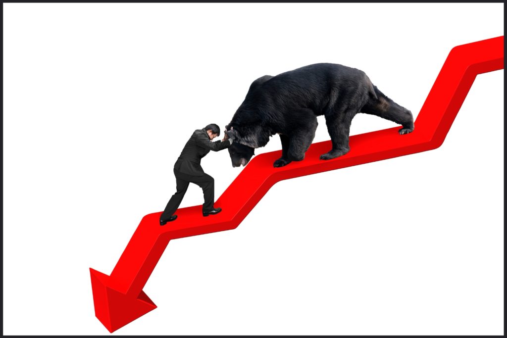 Image of a business person standing on a downward trend lining, pushing against a bear marching down the line.