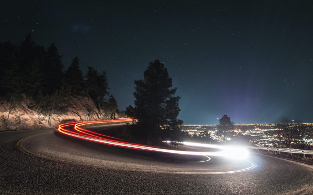 Time lapse phot of a car taking a sharp bend in a two-lane road.