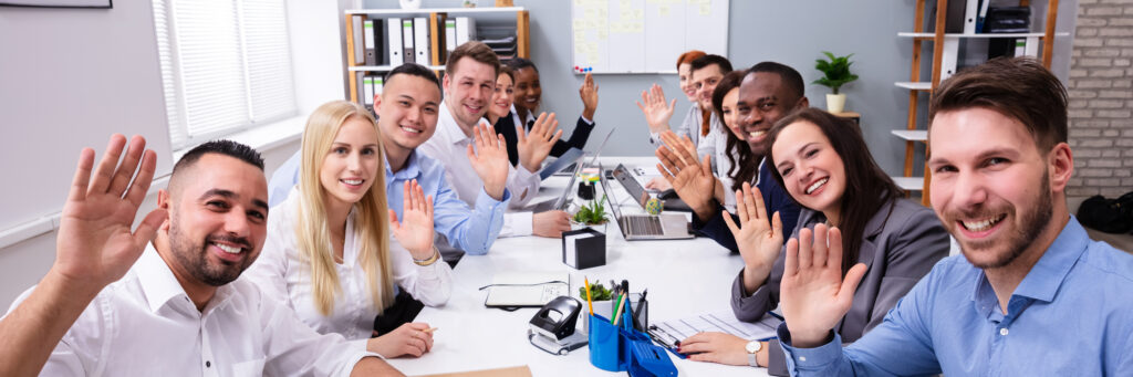 Image of a table full of young business people, all waving in greating.