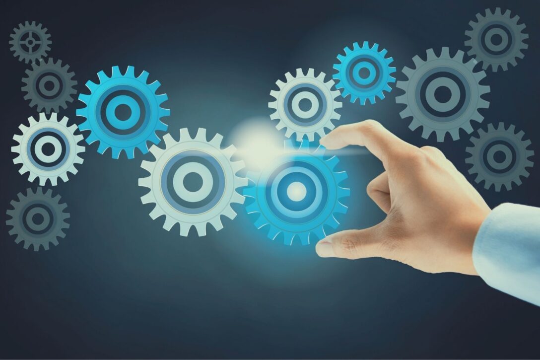 multi-colored gears on a dark background with a hand touching one gear