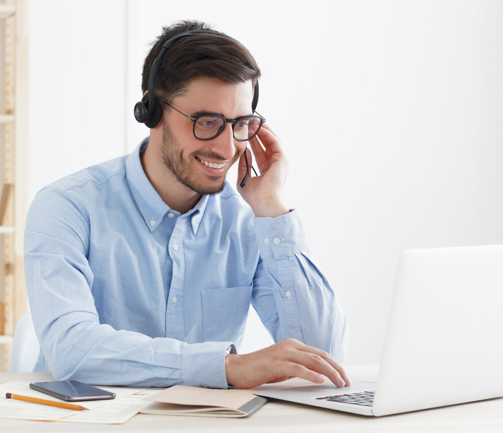Positive guy working in customer support service answering voice call from client, giving instructions and smiling at joke while looking at laptop screen