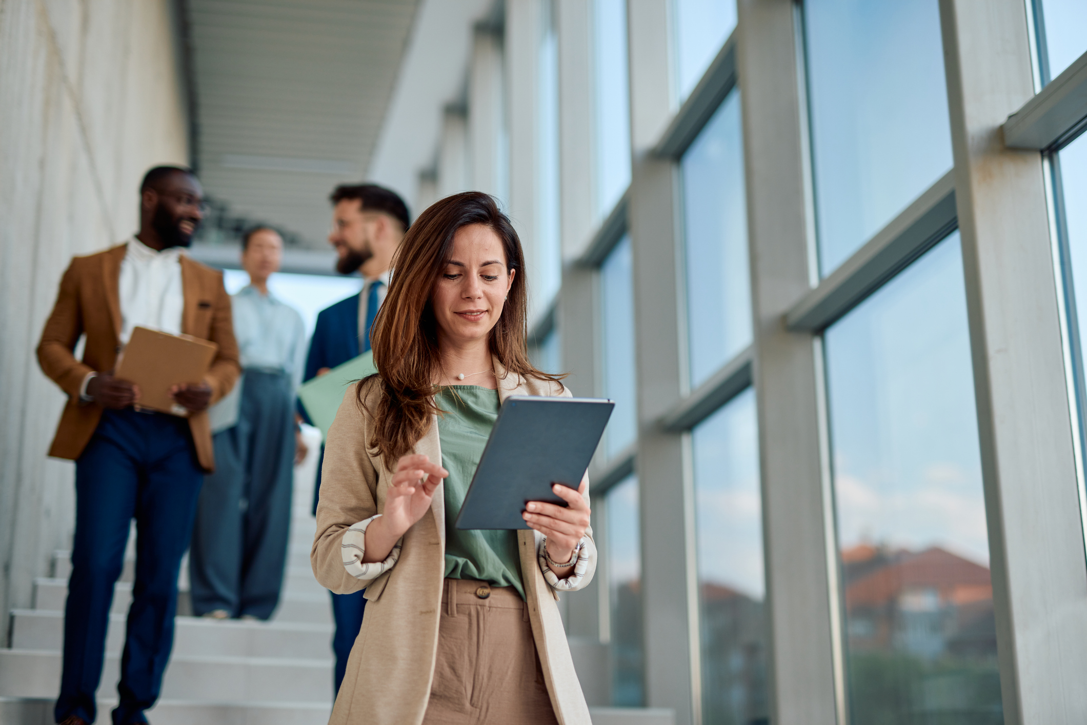 Businesswoman using digital tablet while walking in office hallway with colleagues