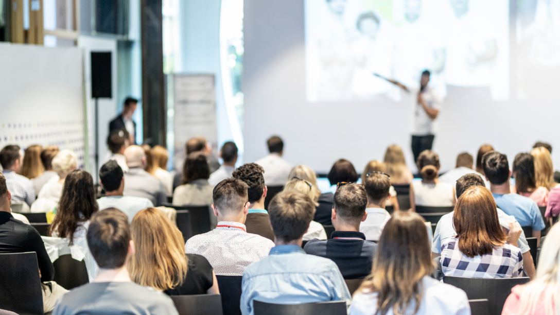 People sit in the audience and listen to a speaker at a conference or event.